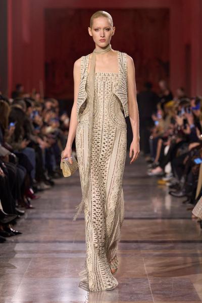 这组细节图展示的是 艾莉·萨博Elie Saab 2026 春夏高级定制系列。整场以裸金、香槟米与沙漠棕为核心色谱，大量珠绣、流苏、立体刺绣与透明层叠工艺构成极致奢华视觉。礼服宛如被阳光照耀的古文明遗迹，在轻纱与晶体装饰之间释放神殿般神圣气息。品牌延续中东高定擅长的华美叙事，同时加入自然植物纹样，使浪漫主义拥有更具史诗感的表达。——来自顽石频道国际流行趋势分析。